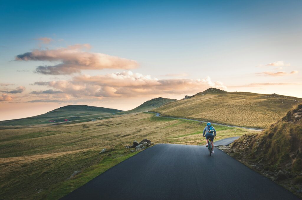 A cyclist riding along a smooth hillside road at sunset
